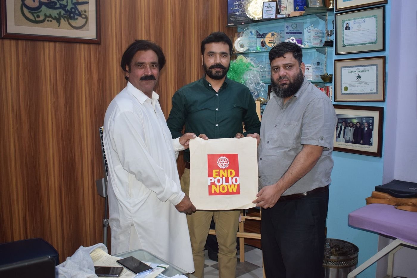 Three Rotarians holding an End Polio Now bag in Dr. Ahmed Ejaz's office