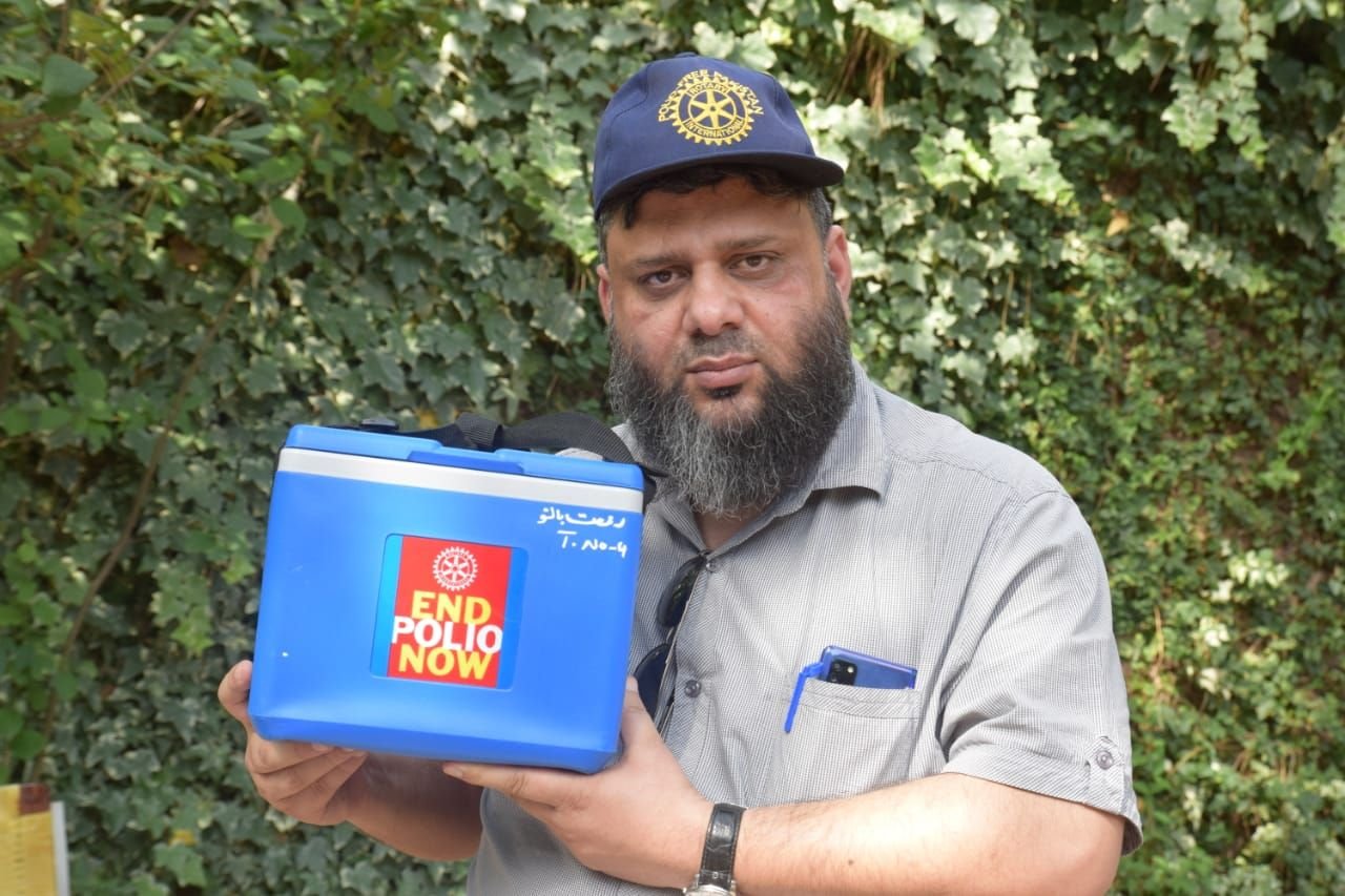 Dr. Ahmed Ejaz in a Rotary cap holding a polio vaccine carrier marked End Polio Now