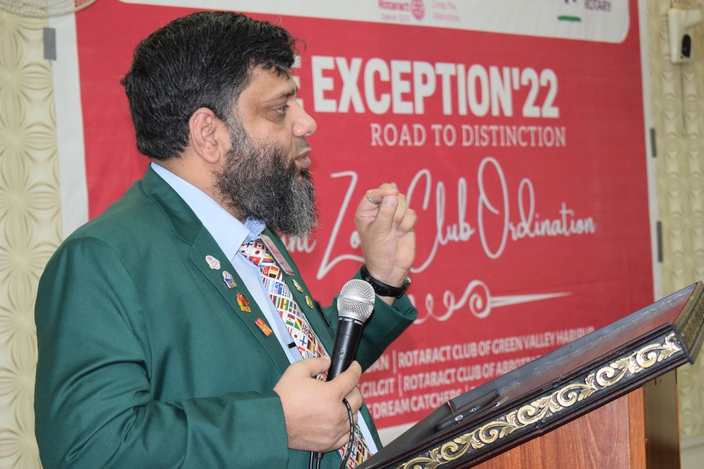 Dr. Ahmed Ejaz in a green Rotary blazer speaking at a podium at The Exception 22 Rotaract event