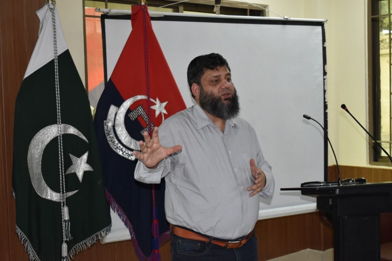Dr. Ahmed Ejaz gesturing while leading a training session beside the Pakistan flag